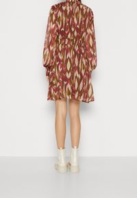 Tryckt miniklänning med långa, puffiga ärmar, utsvängd midja och ett flerfärgat mönster av bruna, rosa och krämfärgade toner. Krämfärgade ankelstövlar.