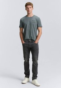 Siva majica z okroglim izrezom s potiskom "Denim Crew" v temni barvi, kombinirana s temnimi kavbojkami in belimi supergami. Priložnostna, oprijeta zasnova.