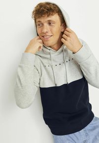 Sudadera color bloqueada en gris y azul marino con capucha ajustable. Presenta un logo en el pecho y puños acanalados. Textura de tela suave.