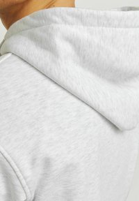 Lichtgrijze hoodie gemaakt van zacht, textuurstof. Heeft een ontspannen capuchon die comfortabel over de schouders valt.