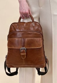 Brown leather backpack featuring a structured design, front pocket with buckle detail, and adjustable black fabric straps.