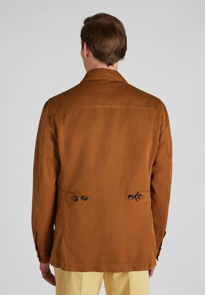 Chaqueta de algodón marrón con corte recto, detalles de botones en la parte trasera y un cuello estructurado. Textura suave y diseño minimalista.