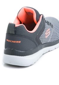 Basket grise Skechers avec une tige en mesh et des accents corail. Dotée d'un col rembourré, d'une poignée et d'une semelle extérieure en caoutchouc blanc.