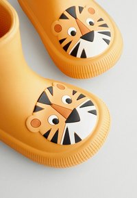 Bottes en caoutchouc jaunes ornées d'un visage de tigre ludique sur le bout, avec des détails en noir et blanc et des semelles texturées pour une meilleure adhérence.
