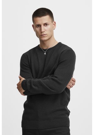 Mørkegrå strikket genser med rund hals, ribbestrikkede mansjetter og kant. Har en sideetikett, og modellen har på seg et sølvanheng.