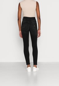 Jeans ajustados negros de cintura alta con una textura lisa, que cuentan con dos bolsillos traseros y un pequeño detalle de logo en la cintura.