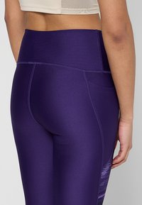 Leggings viola con una finitura testurizzata, vita alta e tasca laterale, caratterizzati da un delicato design in gradiente sulla gamba esterna.