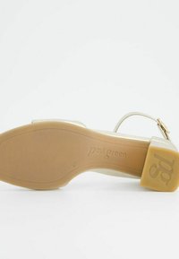Světle béžové kožené sandály se zlatou přezkou, čtveratou špičkou a nízkým pevným podpatkem. Podešev je hladká s jemně embosovaným logem.