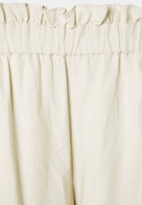 Helle Leinenstoff in Cremefarbe mit gerafftem elastischem Bund und dezentem Rüschendetail am oberen Rand.