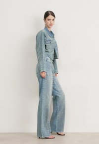 Denim odijelo koje uključuje skraćenu jaknu i široke hlače, obje ukrašene rhinestones, u svijetloplavoj boji. Glatka tekstura s vidljivim šavovima.