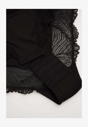 SSujetador de encaje negro con bordes ondulados y cierre de gancho y ojo sobre un fondo claro.