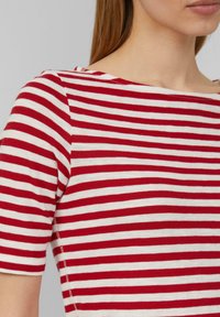 Haut à manches courtes rouge et blanc à rayures avec un décolleté bateau. Matériau en coton doux avec des coutures visibles le long des bords.