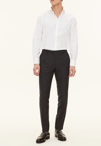 Weißes Langarmhemd kombiniert mit dunkelgrauen, maßgeschneiderte Hose und schwarzen Slippern. Glattes Baumwollmaterial, klassischer Schnitt und subtile Details.