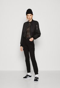 Μαύρο κοντό bomber μπουφάν με λεία υφή, συνδυασμένο με μαύρη cargo παντελόνια με τσέπες και μαύρα sneakers Adidas με λευκές λεπτομέρειες.