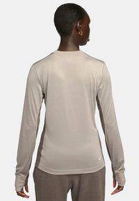 Vaalean beige pitkähihainen urheilupaita, jossa on sileä pinta, pyöreä pääntie ja vartalonmyötäinen muotoilu. Nike-logo alaosassa selässä.