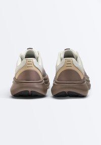 Para beżowych i brązowych butów sportowych widzianych od tyłu, z grubymi, wygodnymi podeszwami i wierzchami z siateczkowej tkaniny.
