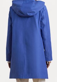 Prenda exterior impermeable azul con capucha, que presenta un diseño sencillo y una textura suave. La prenda es ligeramente más larga y de corte recto.