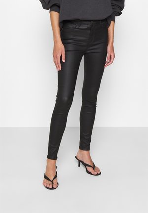 Jeans skinny de piel sintética negra con cintura alta, textura suave y corte ajustado, combinados con chanclas de tacón negras.
