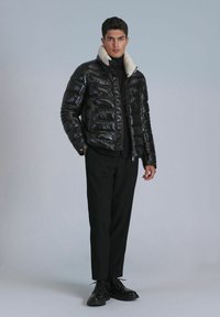 Black puffer jacket with a zip front, featuring a contrasting white fur collar. Paired with black trousers and lace-up shoes. Smooth texture.