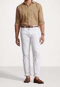 Tan linne långärmad skjorta, vita jeans, brunt läderbälte och loafers. Klassisk passform med knäppning i kragen och uppvikta ärmar.