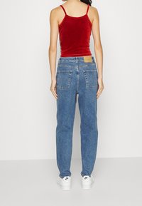 Canottiera di velluto rosso abbinata a jeans in denim chiaro a vita alta con due tasche posteriori e sneakers bianche con dettagli neri.