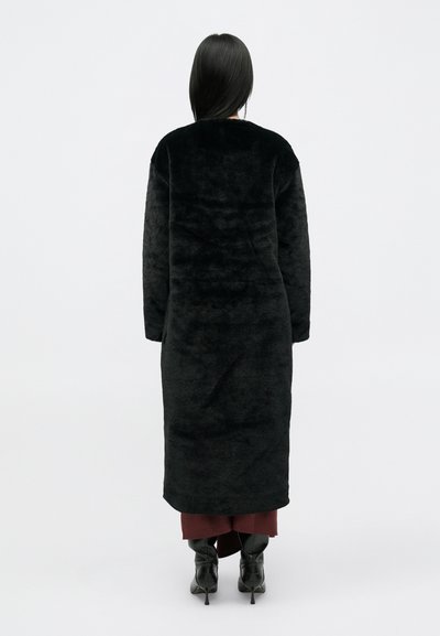 Dugi crni kaput od plišane tkanine, opuštenog kroja, s okruglim izrezom i dugim rukavima, koji seže do sredine listova.