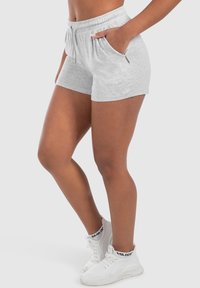 Pantaloni corti in cotone grigio con vita elastica, cordino e tasche laterali. Indossati con sneakers bianche caratterizzate da un design testurizzato.