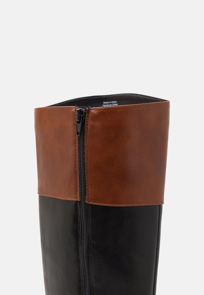 Bottes en cuir montantes avec une partie inférieure noire et un dessus en cuir marron, dotées d'une fermeture éclair sur le côté et d'une texture lisse.