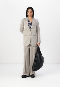 Heled hall ülikond, millel on lõikega krae ja kaks nuppu, koos tumesinise mustriga särgiga. Must tekstuuriga kott. Sagedased mustad jalanõud.