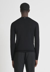 Maglione nero a maglia con maniche lunghe, scollatura rotonda e polsini a costine. Presenta un piccolo etichetta sul retro del collo. Texture liscia.