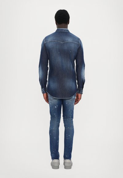 Denim shirt and jeans, both in dark blue. Shirt features two back yokes and button cuffs. Jeans have a distressed finish with white paint splatters.