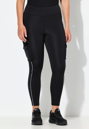 Kvinde iført sorte høj talje leggings med sidelommer cargo og refleksstriber, kombineret med sorte Reebok sneakers.