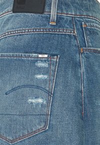 Jeans i ljusblå denim med slitna detaljer. Har en läderetikett i midjan och röd sömnad på fickorna och sömmarna.