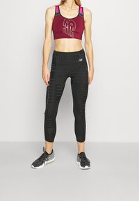 Reggiseno sportivo color bordeaux con design grafico e dettagli rosa, abbinato a leggings neri a cropped con texture, caratterizzati da motivi geometrici e un logo.