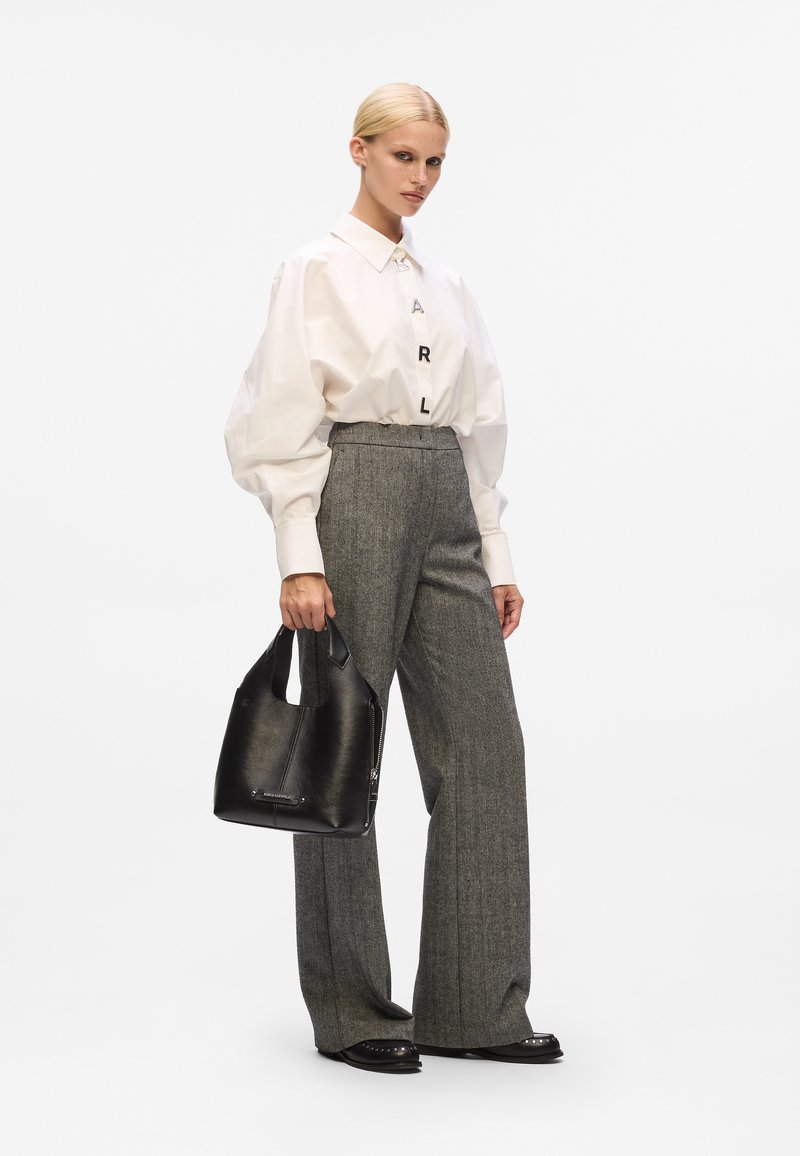 Chemise blanche oversize avec accents de lettres, pantalon gris taille haute, et sac à main en cuir noir avec une anse courbée et des finitions en argent.