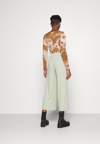 Långärmad tie-dye topp i brun och kräm, kombinerad med vida mintgröna byxor, kompletterad med svarta ankelstövlar.