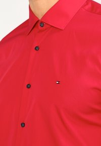 Rode button-up shirt van gladde stof, met zwarte knopen en een klein logo op de linkerborst. Klassiek kraagontwerp.