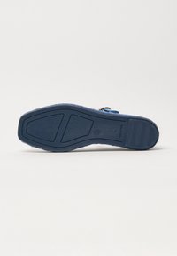 Suola di scarpa blu navy con grip testurizzato, tacco in gomma e cinturino con fibbia visibile su sfondo bianco semplice.