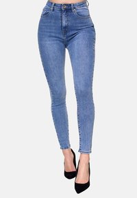 Jeans skinny de talle alto en un denim azul de lavado medio con cinco bolsillos y cremallera, combinados con tacones de aguja negros.