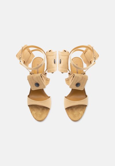 Μπεζ σανδάλια ανοιχτών δακτύλων με λουράκια στον αστράγαλο, διπλούμενες υφασμάτινες θήκες κοντά στον αστράγαλο και εσωτερικές σόλες που μοιάζουν με σουέντ.