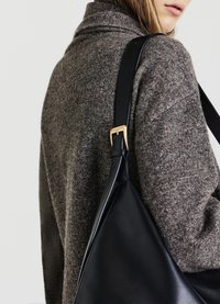 Borsa in pelle nera con una larga tracolla e dettagli in fibbia dorata, abbinata a un maglione marrone dalla texture particolare. La borsa ha una forma triangolare.