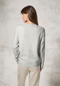 Pull en maille gris clair avec un col et un ourlet côtelés. La texture semble douce, associé à un pantalon de couleur claire dans une teinte complémentaire.