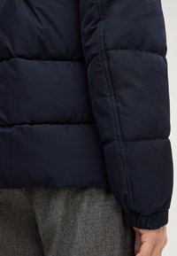 Giacca a puffo navy con design trapuntato, polsini elasticizzati e finitura liscia. Cuciture visibili e imbottitura morbida.