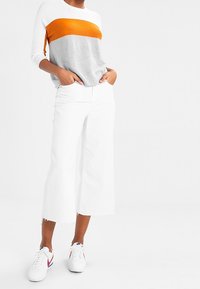 Pull en tricot à rayures horizontales orange, grises et blanches ; associé à un jean blanc large raccourci et des baskets blanches avec des accents rouges.