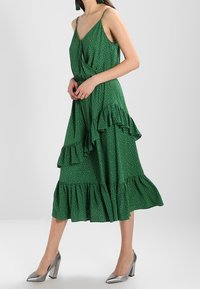 Green dress with adjustable spaghetti straps, layered ruffles, and white polka dots. Worn with silver high-heeled shoes.