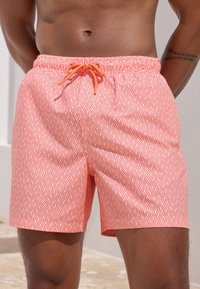 Badeshorts i en koralfarvet nuance med bølgemønster, udstyret med elastik i taljen og justerbar snøre. Midt på låret, letvægtsstof.