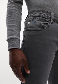 Jeans in denim grigio con una vestibilità slim, caratterizzati da una leggera elasticità, tasche frontali e un logo ricamato blu sulla tasca posteriore.