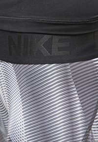Cinturilla atlética negra con el logo "NIKE" en relieve sobre una tela gris y blanca con un patrón de líneas diagonales y varias texturas.