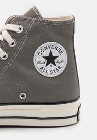 Szare canvasowe sneakersy typu high-top z białymi oczkami i sznurowadłami, z okrągłą czarno-białą naszywką z gwiazdą. Gumowa podeszwa z czarnymi akcentami.