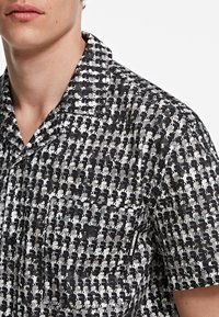 Camicetta a maniche corte con un motivo grafico in bianco e nero, realizzata in tessuto leggero con colletto classico e una piccola etichetta con logo.